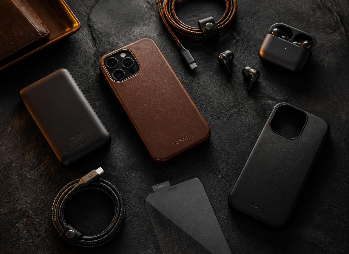 Phone cases, cables, earbuds and a power bank arranged on a dark surface